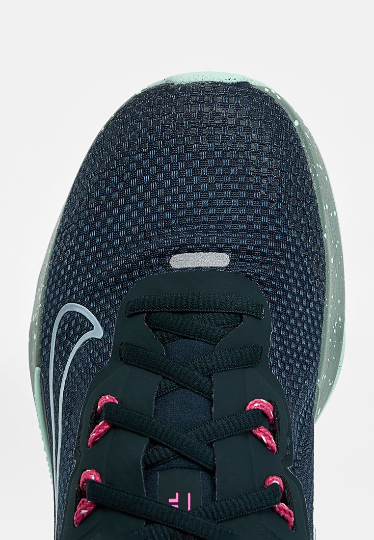 Zapatilla deportiva de malla azul marino con cordones rosas y una suela exterior moteada en verde menta, con una parte superior texturizada y un detalle reflectante de la marca.