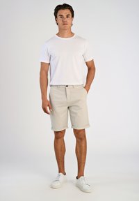 Beige shorts dengan ujung yang digulung, penutupan kancing, dan saku samping, dipadukan dengan kaos putih polos berkerah bulat dan sepatu kets putih.