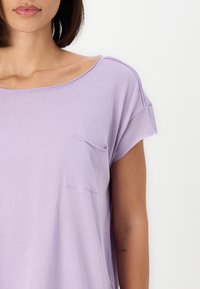 Licht lavendelkleurig t-shirt met korte mouwen, gemaakt van zacht stof, met een ronde halslijn en een klein borstzakje. Soepele, ontspannen pasvorm.