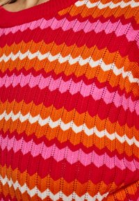 Maglione lavorato a maglia con motivo a zigzag in rosso, rosa, arancione e bianco. La texture è a coste con colori e forme notevolmente variabili.