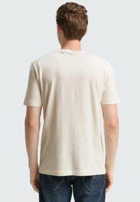 Beżowa koszulka z krótkim rękawem i okrągłym dekoltem, wykonana z miękkiego materiału, o gładkiej fakturze i prostym wzorze, widoczna od tyłu.