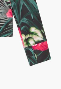 Tessuto dei leggings con stampa di foglie e fiori tropicali in verde, crema e rosa brillante su sfondo nero, che mostra l'orlo del pantalone piegato.