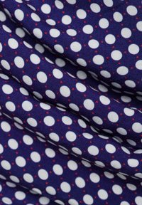 Tessuto blu navy con pois bianchi e piccoli accenti rossi, caratterizzato da una trama liscia e pieghe discrete, creando un aspetto a strati.