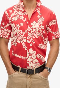 Camisa roja de manga corta con botones y estampados blancos de flores y hojas, con cuello puntiagudo y ajuste relajado.