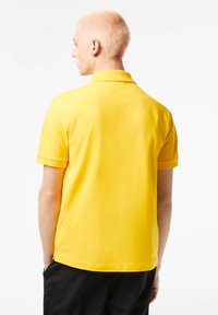 Polo giallo con maniche corte, colletto piatto e una texture liscia. Cuciture visibili e orlo leggermente curvo sul retro.