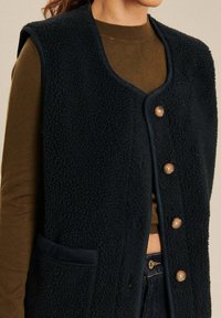 Marine fleece vest met een gestructureerd oppervlak, met een V-hals, vijf houten knopen en een zak aan de linkerkant.