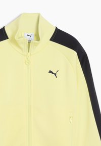 Gul zip-up jacka med svarta sidpaneler. Inkluderar en hög krage, en ficka med dragkedja fram och en svart Puma-logotyp på bröstet.