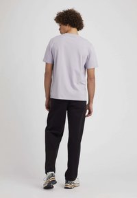 T-shirt court à manches courtes de couleur violet clair, coupe décontractée, associé à un pantalon noir. Baskets décontractées avec un design blanc, doré et noir.