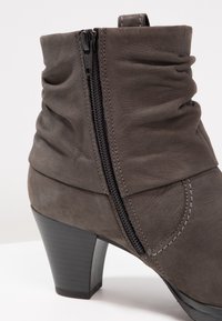 Bottine en cuir gris avec texture froncée, fermeture éclair latérale et talon empilé noir. Caractéristiques coutures renforcées et finition lisse.