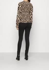Top a maniche lunghe con stampa leopardata e dettaglio arricciato sul retro, pantaloni neri aderenti e stivaletti neri con tacco.