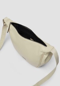 Beżowa skórzana torebka na ramię o gładkiej fakturze, z zamknięciem na suwak i czarnym wnętrzem. Posiada pleciony pasek z logo.