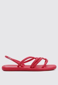 Sandalias de goma rojas con múltiples correas entrelazadas y una suela plana. Textura suave, diseño minimalista y el logo de la marca visible en el lateral.