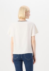 Top bianco a maniche corte con finitura testurizzata e dettaglio del collo nero, abbinato a jeans di denim blu con design della tasca cucita classico.