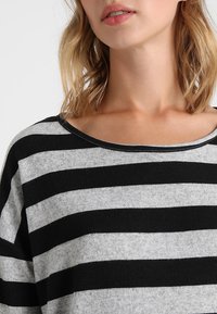 Czarny i szary sweter w paski z okrągłym dekoltem i luźnym krojem. Miękka tekstura, widoczne szwy wzdłuż dekoltu i rękawów.