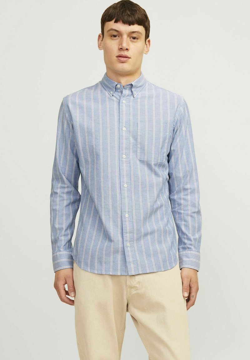 Šviesiai mėlynas marškiniai su plonomis vertikaliomis baltomis ir rožinėmis juostelėmis, su vienu kišenės projektu krūtinėje ir ilgomis rankovėmis.