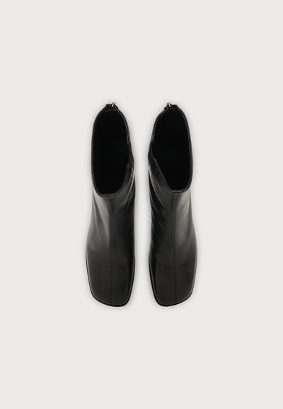 Paire de bottines en cuir noir à bouts carrés et fermetures éclair latérales, vues de dessus sur un fond clair.