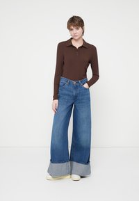 Camisa polo de rayas marrón con mangas largas, combinada con unos vaqueros de mezclilla azules amplios y acampanados, con dobladillo y puños contrastantes.