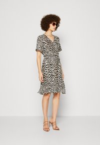 Robe à motif léopard en tissu léger, avec des manches courtes, un décolleté en V, une taille cintrée et un ourlet évasé ; assortie à des sandales à talons beiges.