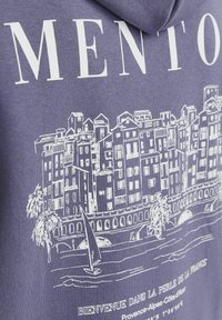 Sudadera morada con un gráfico blanco de un paisaje costero, un velero pequeño, palmeras y el texto: "Bienvenido a la perla de Francia."