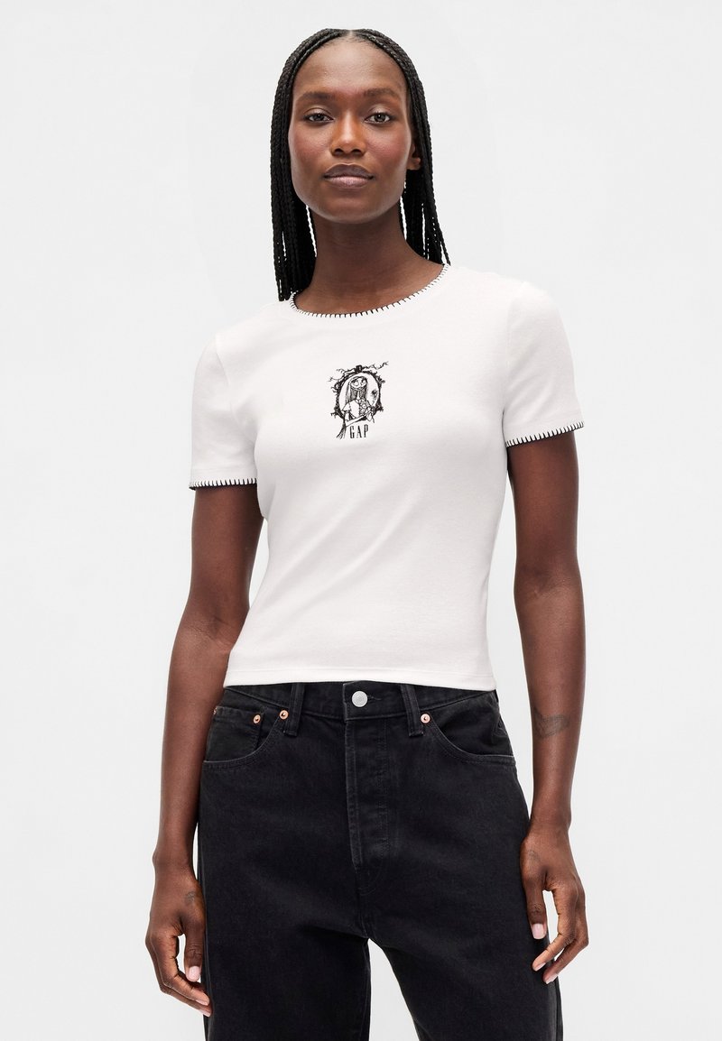 Hvit bomulls-T-skjorte med korte ermer, med et svart grafisk trykk og broderte detaljer rundt halsen, kombinert med svarte jeans.