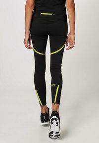 Černé sportovní legíny s reflexními žlutými detaily a zipy na kotnících. Vyrobeno z elastického, vlhkost odvádějícího materiálu pro pohodlí.