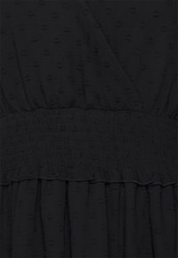 Schwarzes Kleid aus strukturiertem Stoff mit erhabenen Punkten, einer gerafften Taille und einem Rüschensaum, das ein geschichtetes Design zeigt.