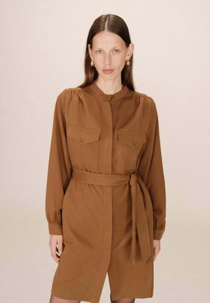 Robe marron ceinturée avec col, manches longues et deux poches poitrine. Fabriquée en tissu texturé, présentant une fermeture à boutons sur le devant.