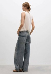 Lichtgewicht, mouwloos topje in crème, gecombineerd met oversized, vervaagde blauwe jeans met een rechte pijp en subtiele achterzakken.