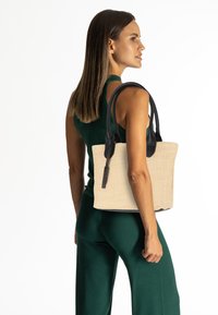 Sac fourre-tout en fibres naturelles avec poignées en cuir noir. Présente un corps texturé beige et une forme rectangulaire structurée pour un style moderne.