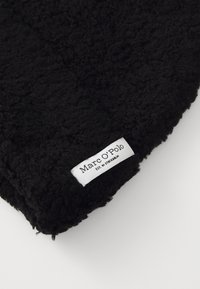 Zwart, gestructureerde stof met een pluche, donzige uitstraling. Bevat een wit etiket met de tekst "Marc O'Polo" en merkdetails.