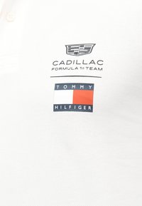 Λογότυπο της ομάδας Cadillac Formula 1 και σημαία Tommy Hilfiger σε κόκκινο, άσπρο και ναυτικό μπλε σε υφασμάτινη βάση με υφή.