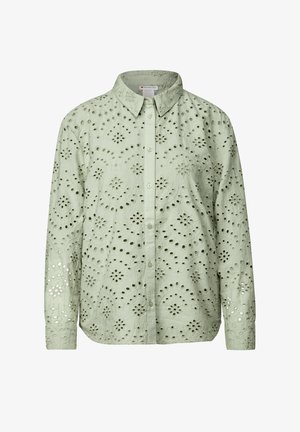 Camisa verde claro con cuello estructurado y mangas largas, hecha de una tela con intrincados patrones cortados en todo su diseño.