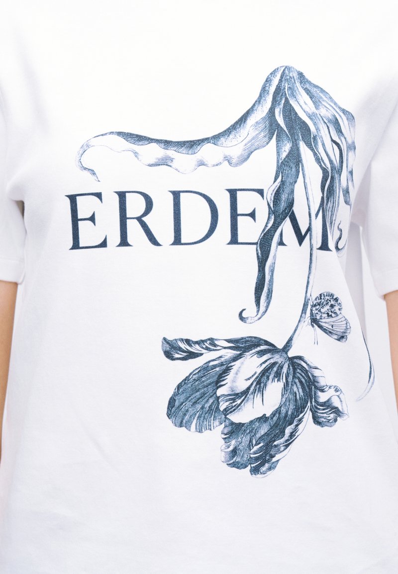 Wit T-shirt met een donkerblauwe botanische illustratie van een tulp en een vlinder bovenop het gedeeltelijk zichtbare woord "ERDEM."