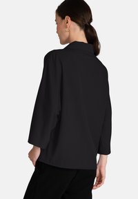 Blusa nera a maniche corte con taglio diritto, colletto a risvolto e tessuto liscio. La vista posteriore mostra un design semplice e una vestibilità comoda.