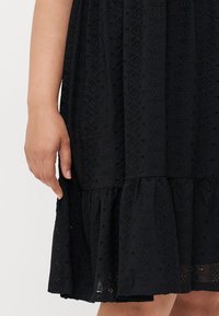 Black dress with textured fabric featuring intricate patterns. The skirt has a ruffled hem and the fabric shows a layered design.