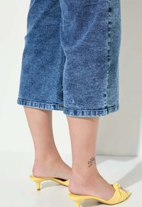 Džínové culotte šortky v bledě modré barvě, s uvolněným střihem a roztrhanými okraji. V páru s žlutými sandály na podpatku, které mají uzlový design.