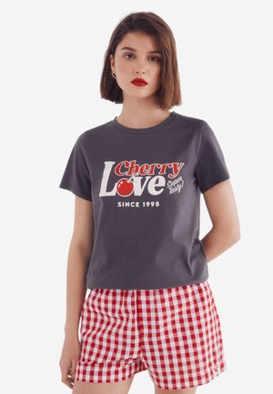 Gray cotton t-shirt with red and white "Cherry Love" graphic; paired with red and white gingham shorts, showcasing a casual summer look.