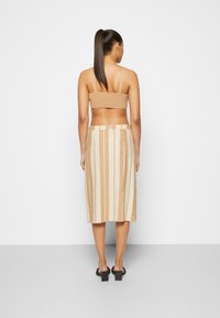 En tan ribbad bralette parat med en midjelång beige och krämfärgad randig kjol, som visar upp en jämn textur och inga synliga knäppningar.