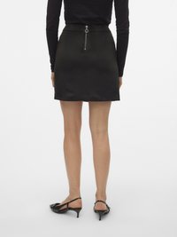 Zwarte aansluitende rok met een gladde afwerking, voorzien van een ritssluiting aan de achterkant en een hoge taille. Gecombineerd met zwarte slingback schoenen.