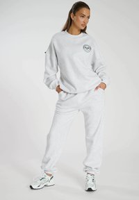 Grauer Sweatshirt mit rundem Ausschnitt und schwarzem Logodetail, kombiniert mit passenden grauen Sweatpants mit elastischen Bündchen. Sneakers mit grünen Akzenten.