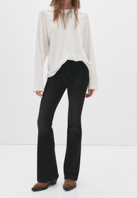 Haut blanc à manches longues avec une coupe ample, associé à un jean évasé noir. Bottes marron à talons avec des bouts pointus. Design simple et épuré.