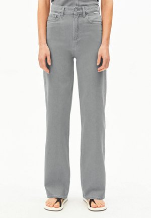 Graue Jeans mit geradem Bein und hoher Taille, getragen mit schwarz-weißen Flip-Flops, von der Taille bis zu den Füßen vor weißem Hintergrund gezeigt.