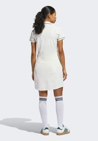 Weißes Kleid mit Polokragen, kurzen Ärmeln und schwarzem Besatz. Kombiniert mit kniehohen weißen Socken mit Marineblauen Streifen und schuhen mit grünen Akzenten.