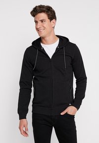 Zwarte zip-up hoodie van zachte stof, met een trekkoordcapuchon, twee voorste ritszakken en ribgebreide boorden en zoom.