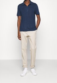 Námořnická modrá polo tričko s krátkými rukávy, s límečkem a knoflíkovou légou, doplněné světlými béžovými kalhotami a bílými teniskami.