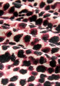 Tissu en polaire présentant un motif léopard rose et noir, avec une texture douce et des taches floues distinctes sur fond crème.