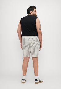 T-shirt sans manches noir, short léger rayé avec des bandes bleues et foncées, vue de dos, avec poches, associé à des baskets blanches.