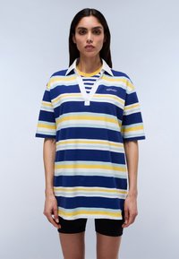Polo rayé en bleu, jaune et blanc, à manches courtes, avec un col blanc et un décolleté en v. Présente un petit logo sur la poitrine.