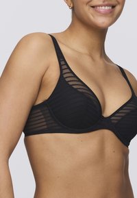 Musta rintaliivi, jossa on läpinäkyviä pannuita, uritettua tekstuuria, kolmiomuotoiset kupit ja säädettävät hihnat. Sisältää tukevan langan.