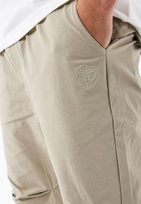 Pantalones beige con una textura suave, con un sutil logo bordado en el lateral y un ajuste relajado para mayor comodidad.